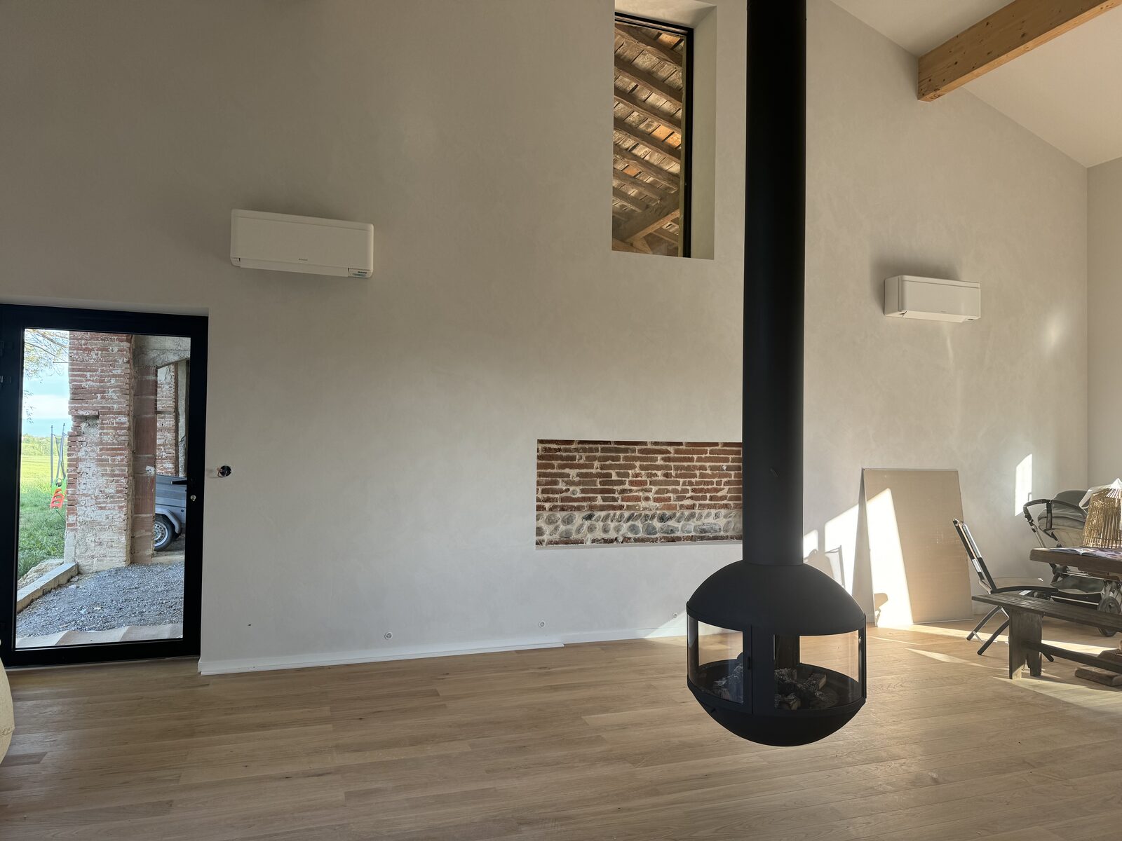 Deux climatiseurs split Daikin blancs installés en hauteur dans un séjour cathédrale avec poêle central, rénovation d'une ferme près de Balma