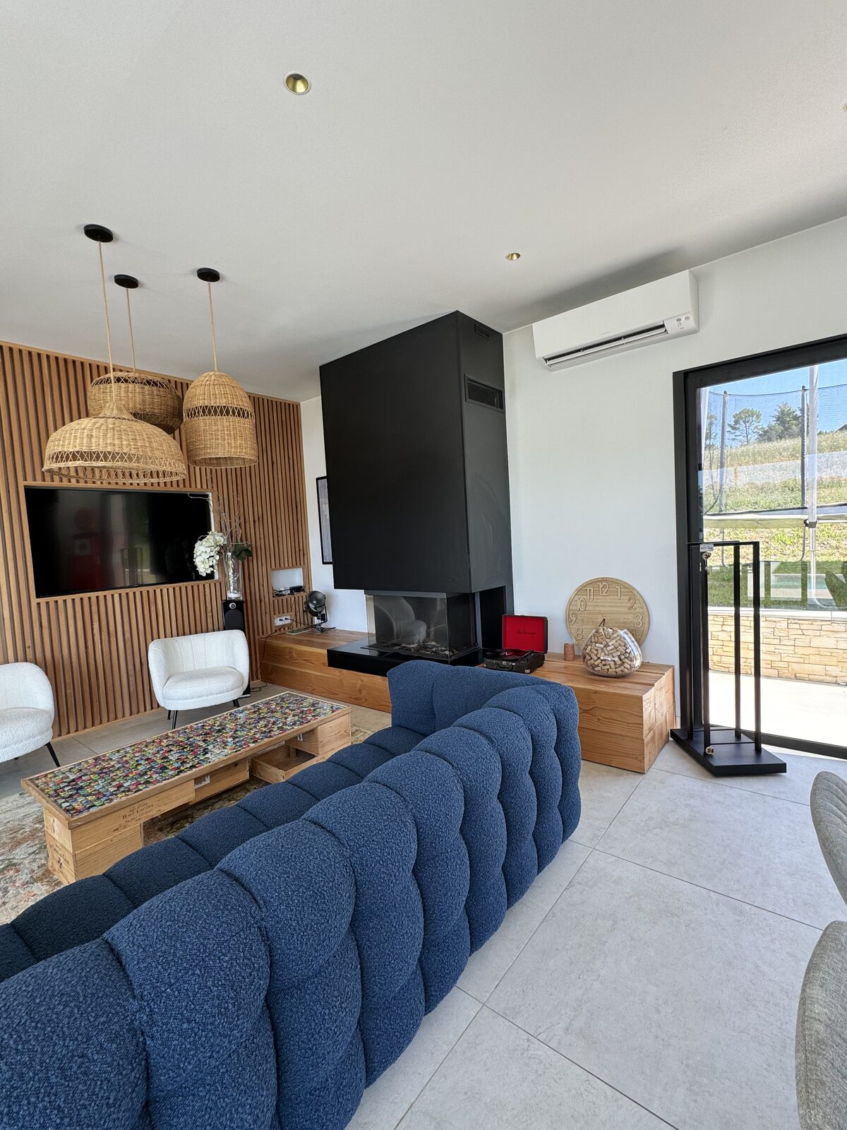 Climatiseur split Daikin blanc installé au-dessus d'une baie vitrée dans un salon moderne avec cheminée noire design